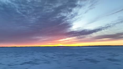 Drone-flight-over-a-frozen-lake-and-beautiful-clouds-at-sunset