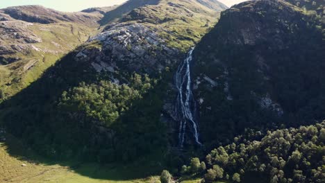 Aerial-panoramic-natural-drone-environment-Steall-Waterfall,-Ben-Nevis,-Scotland-stream-falling-at-green-countryside-valley-fields