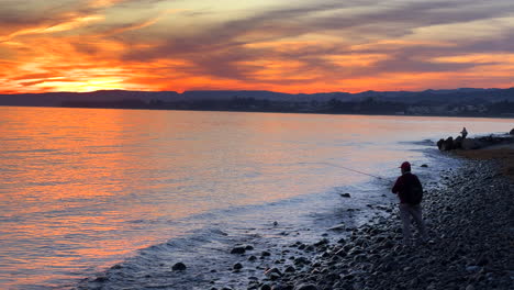Leute,-Die-Am-Strand-Angeln,-Mit-Einem-Unglaublichen-Orangefarbenen-Sonnenuntergangshimmel-In-Marbella-Estepona,-Spanien,-Tolle-Aussicht,-Ruhige-Meereswellen,-4K-Aufnahme
