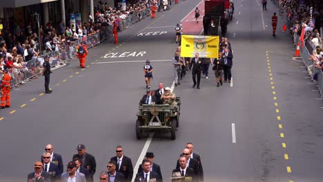 Senior-veteran-riding-on-military-Willys-jeep,-driving-down-the-street-participating-the-annual-Anzac-Day-parade,-waving-at-the-cheering-crowds,-handheld-motion-close-up-shot