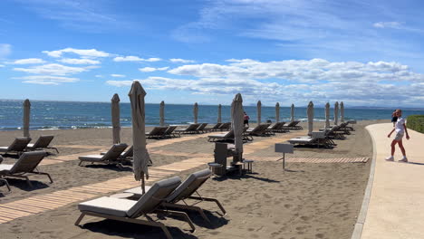 Beautiful-beach-day-in-the-sunny-Estepona-beach-with-sun-beds,-sea-view,-sand-and-blue-sky,-holiday-vacation-in-Spain,-Paseo-Maritimo,-4K-shot