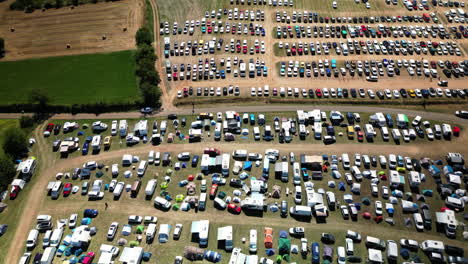 Kreisförmige-Luftaufnahme-Eines-Vollen-Campingparkplatzes-Mit-Grüner-Wiese-Und-Rennstrecke-Im-Hintergrund-Beim-Musikfestival