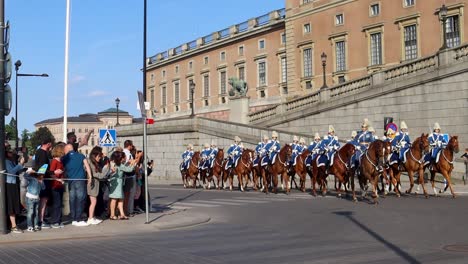 Royal-guards-in-uniform-ride-horses-by-Swedish-Royal-Palace-on-National-day,-slo-mo