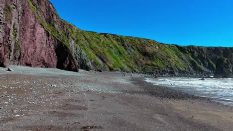 Gente-Caminando-Por-La-Playa-Con-Acantilados-Erosionados-Y-Cielo-Azul-Playa-Ballydwane-Costa-De-Cobre-Waterford-Irlanda
