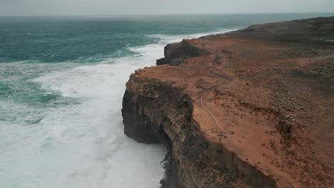 Drone-view-of-ocean-water-hitting-high-grounds-of-Cape-Bridgewater,-Australlia