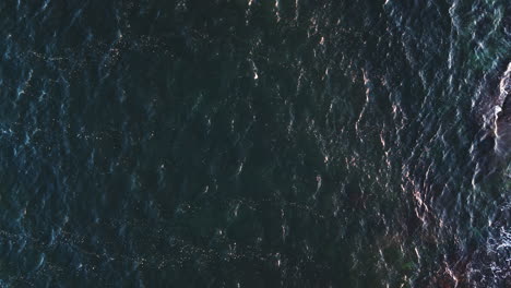 Ocean-wave-current-ripples-across-sea-surface-with-white-glistening-tops,-drone-static