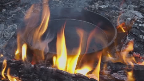 Orange-flames-surround-cast-iron-skillet-being-seasoned-in-open-fire