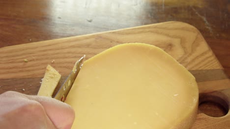 Delicious-hard-dry-cheese-is-sliced-with-small-knife-on-cutting-board