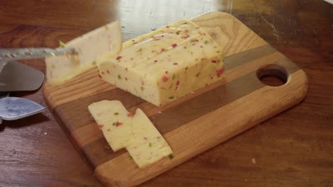 Cheese-knife-used-to-cut-a-slice-of-spicy-red-pepper-cheese-on-block