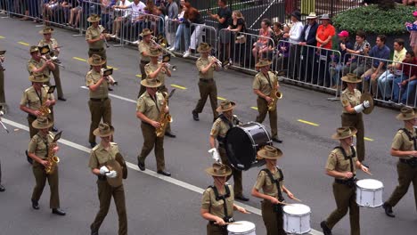 Cuerpo-De-Bandas-Del-Ejército-Australiano-Tocando-Instrumentos-Musicales-Y-Marchando-Por-La-Calle-Adelaida,-Alentado-Por-La-Multitud-Que-Se-Alineaba-A-Los-Lados-Durante-El-Desfile-Del-Día-De-Anzac,-En-La-Ciudad-De-Brisbane.