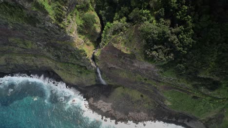 Madeira-Véu-da-Noiva-viewpoint-aerial-view-looking-down-descending-steep-rock-face-towards-waterfall-cascading-into-ocean-below