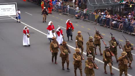 Infantería-Del-Ejército-Australiano,-Soldados-Portando-Rifles-De-Francotirador-Marchando-Por-La-Calle,-Seguidos-Por-Mujeres-Vestidas-Con-Uniforme-De-Enfermería-De-La-Primera-Guerra-Mundial-Que-Participan-En-El-Tradicional-Desfile-Anual-Del-Día-De-Anzac