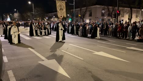 The-procession-goes-in-formation-where-we-see-the-banner-of-the-brotherhood-of-the-Virgin-of-Sorrows-behind-the-Nazarenes-with-children-and-after-the-nuns-in-black-we-see-people-on-the-sides