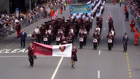 Students-from-St-Peters-Lutheran-College-Indooroopilly-music-band-performing-and-marching-down-the-street-with-cheering-crowds-alongside,-honouring-the-memory-of-those-who-served-during-Anzac-day