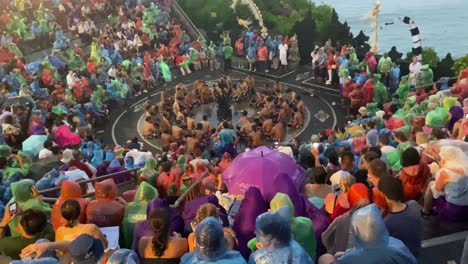 A-large-crowd-of-tourists-watch-a-Kecak-dance-performance-wearing-raincoats-at-Uluwatu-Temple,-Bali,-Indonesia-despite-a-rainstorm