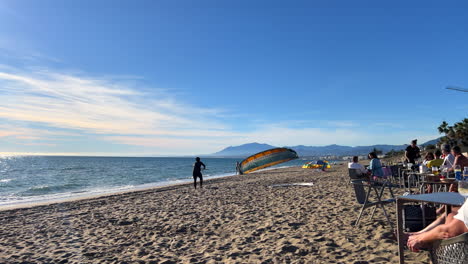 A-kite-surfer-at-the-Marbella-beach-on-a-windy-sunny-day-with-blue-sky,-kiteboarding-kitesurfing-in-Spain,-4K-shot