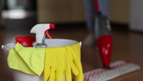 4k-video-footage-detergents-in-a-bucket-on-the-floor-and-woman-cleaning-her-home-in-the-background