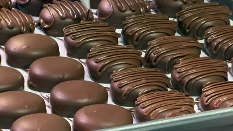 Close-up-of-chocolate-piping-designs-being-squeezed-onto-round-chocolate-sweets-at-a-bakery