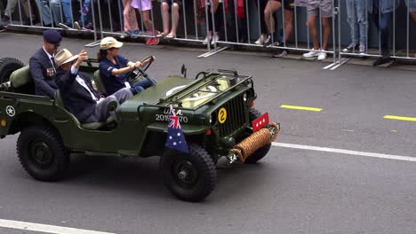 Senior-veteran-riding-on-the-military-jeep,-driving-down-the-street,-participating-the-annual-Anzac-Day-parade,-waving-at-the-cheering-crowds-of-public