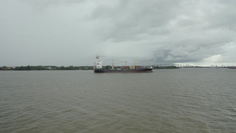Cargo-ship-sailing-in-the-Suriname-river-towards-harbor,-drone-view-ascending-towards-ship