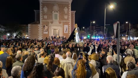 We-see-the-illuminated-parish,-the-Virgin-being-carried-by-her-parishioners,-the-priest-behind-her-and-a-large-crowd-of-people-excited-by-the-procession