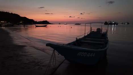 At-sunset,-tranquil-fishing-boats-grace-the-shores-of-Koh-Tao,-Thailand,-as-the-evening-sun-casts-its-golden-rays-upon-the-shimmering-water,-embodying-the-essence-of-travel-and-vacation