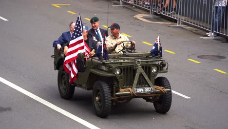 Post-World-War-II-allied-war-veterans-riding-on-the-military-vehicle,-participating-the-annual-Anzac-Day-parade,-waving-at-the-cheering-crowds