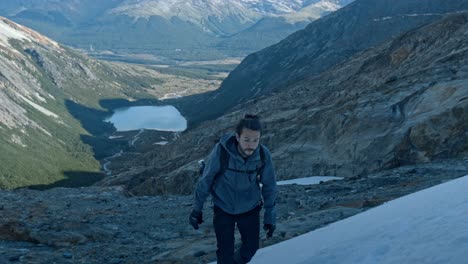 Photographer-hiking-in-to-Ojo-del-Albino-glacier-in-Ushuaia,-Argentina-with-Laguna-Esmeralda-in-the-background