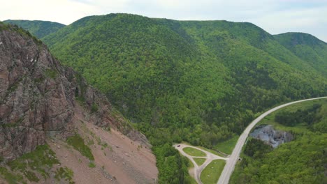 Wide-angle-drone-shot-revealing-the-beautiful-mountains-on-the-world-famous-Cabot-Trail-drive-with-massive-mountains-surrounding-a-small-road-in-Nova-Scotia,-Canada