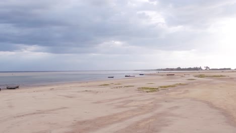 Aerial-drone-footage-captures-a-wet-sandy-beach-during-low-tide-in-Colombia,-with-a-stunning-sunset-in-the-background-and-some-boats-parked-on-the-sand