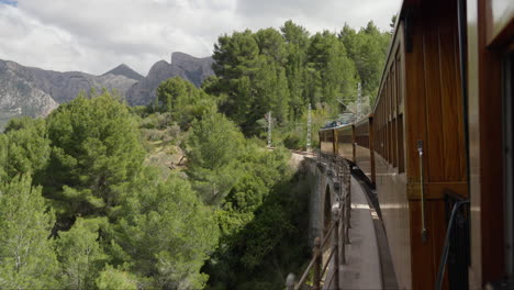 Vintage-train-crossing-a-bridge-in-Soller,-Mallorca-with-scenic-backdrop