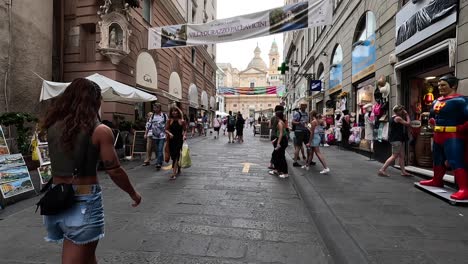 Handheld-clip-walking-along-busy-paved-street-lined-with-shops-and-restaurants-in-Italy