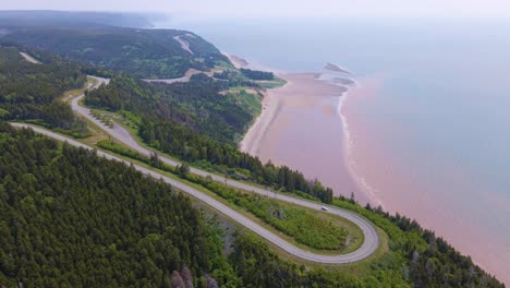 Aerial-shot-of-one-of-the-most-famous-landscapes-in-Canada-located-at-the-Bay-of-Fundy-trail-in-New-Brunswick-where-the-highway-is-close-by-the-massive-cliffs-edge-with-the-beach-in-the-background