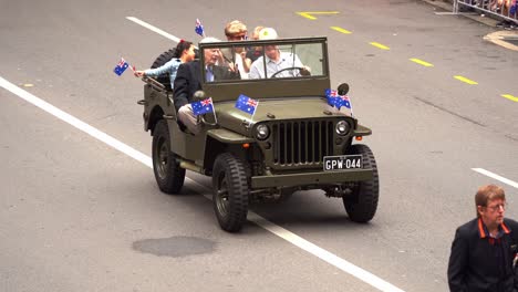 Veteran-and-families-riding-on-the-military-vintage-vehicle-driving-down-the-street,-participating-at-the-Anzac-Day-parade-at-Brisbane-city,-waving-Australian-national-flag-at-the-cheering-crowds