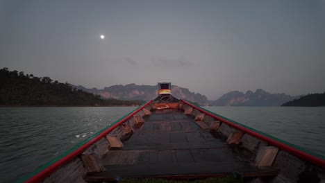 Un-Barco-Deslizándose-Por-Las-Aguas-Del-Parque-Nacional-De-Khao-Sok-En-Surat-Thani,-Tailandia,-Durante-La-Noche,-Con-La-Luna-Brillando-Visiblemente-En-El-Horizonte,-Encarnando-El-Concepto-De-Viajes-Y-Vacaciones.