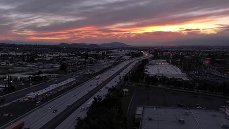 incredible-dynamic-sunset-with-changing-clouds-orange-and-pink-over-California-Highway-10-with-busy-traffic-scene-getting-darker-as-the-sun-sets-AERIAL-DOLLY-PUSH