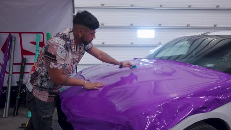 A-Young-Man-installs-purple-vinyl-plastic-wrap-on-a-car-hood-in-a-shop