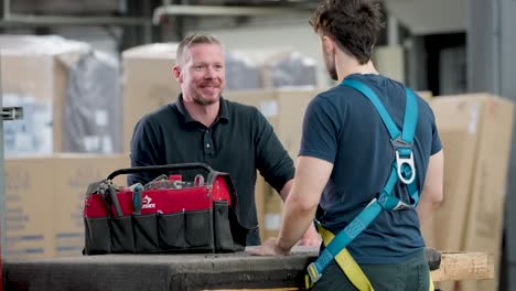 An-older-employee-laughs-and-smiles-while-training-a-young-apprentice-in-a-warehouse