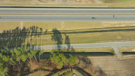 Draufsicht-Auf-Die-Schnellstraße-S6-In-Pommern-In-Der-Nähe-Von-Gdynia,-Polen,-Mit-Dem-Geradlinigen-Straßenabschnitt,-Der-Von-Den-Starken-Silhouetten-Der-Bäume-Gesäumt-Ist