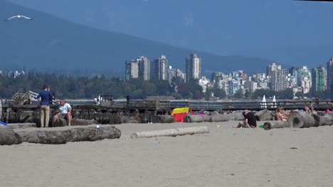 Zwei-Männer-Mit-Großen-Muskeln-Am-Strand-Mit-Segelbooten-Und-Der-Skyline-Von-Vancouver