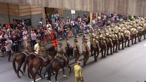 In-Der-Feierlichkeit-Des-Anzac-Day-Marschieren-Australische-Armeetruppen-Die-Straße-Entlang,-Einige-Reiten-Auf-Pferden-Und-Nehmen-An-Der-Jährlichen-Paradetradition-Teil,-Während-Die-Menschenmengen-Entlang-Der-Straße-Jubeln