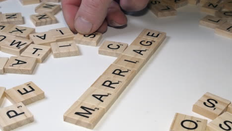 Right-hand-places-Scrabble-tile-letters-onto-table-top:-MARRIAGE-SCAM