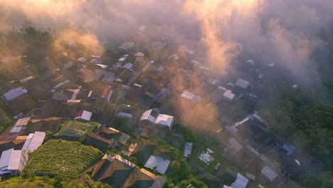 Vista-Aérea-Del-Pueblo-En-Las-Tierras-Altas-Envuelto-En-Niebla-Iluminada-Por-Los-Rayos-Del-Sol-Naciente