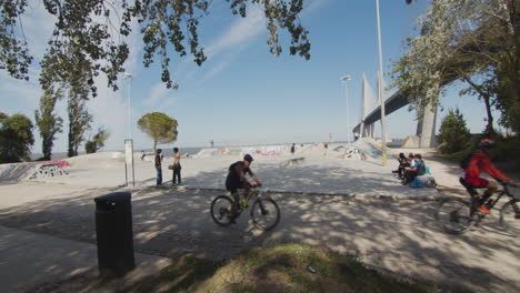 Gente-Patinando-Y-Montando-En-Bicicleta-En-Un-Skatepark-En-Un-Parque-Público-En-El-Parque-Das-Nações,-Lisboa,-Portugal
