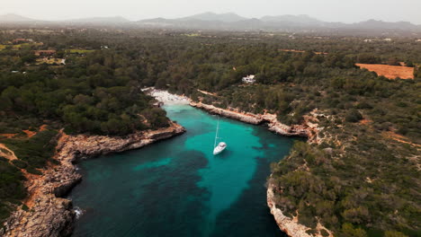 Serene-aerial-view-of-a-yacht-in-the-Cala-Sa-Nau-cove,-Mallorca