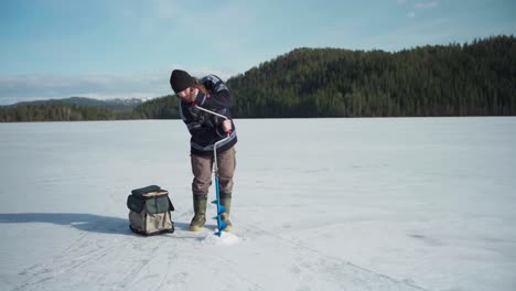 A-Man-With-Hand-Ice-Auger-Drilling-Hole-In-Frozen-Lake-During-Sunny-Day