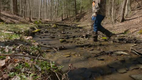 man-walking-in-woods-crossing-a-water-way-of-stream