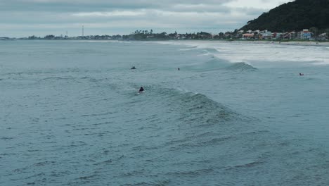 Surfistas-Flotando-En-El-Agua-Mientras-Las-Olas-Se-Los-Llevan,-La-Ciudad-Al-Fondo