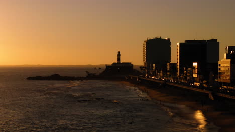 Aerial-view-of-Farol-da-Barra,-the-sea-and-the-neighborhood-around,-at-sunset,-Salvador,-Bahia,-Brazil