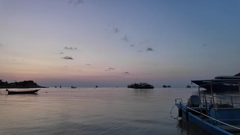 Tranquil-waters-off-Koh-Tao,-Thailand,-the-serene-evening-atmosphere-as-fishing-boats-gently-float-on-the-surface,-while-distant-tour-boats-arrive-at-the-bay,-painting-a-peaceful-scene